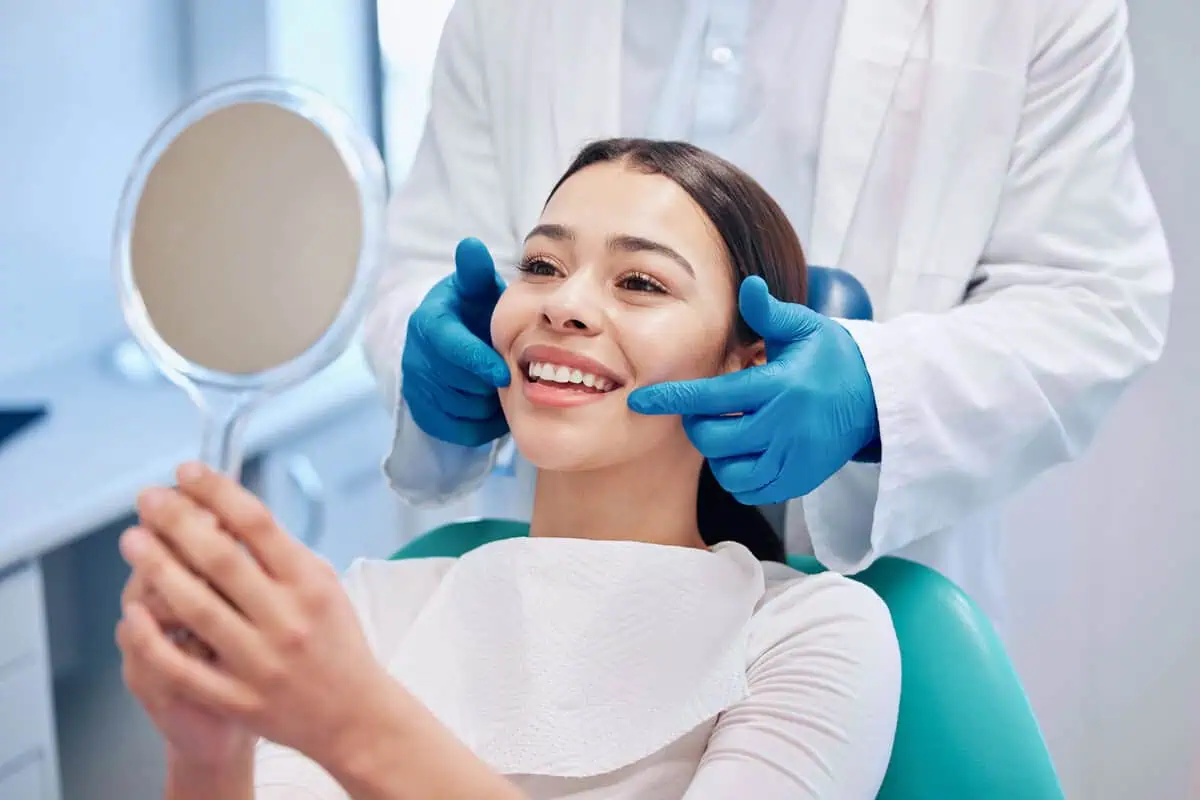 Happy patient with braces smiling into a hand mirror