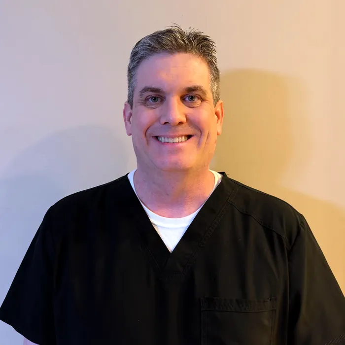 Dr. Devin Croft, orthodontist, smiling in navy scrubs